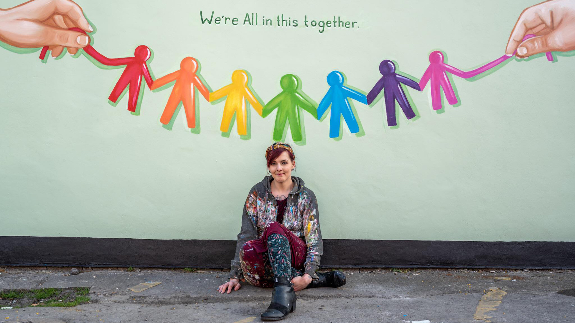 Rachel List sits under one of her murals saying 'We're All In This Together'