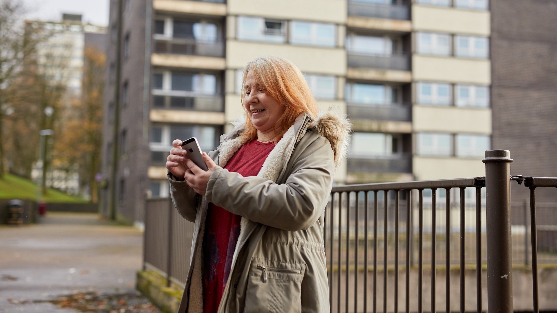 Colette holds her new phone and smiles in front of a block of flats