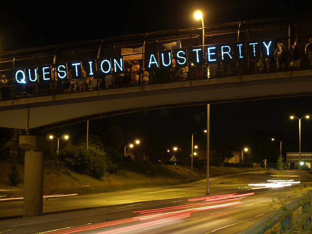 An anti-austerity message is projected onto a pedestrian overpass