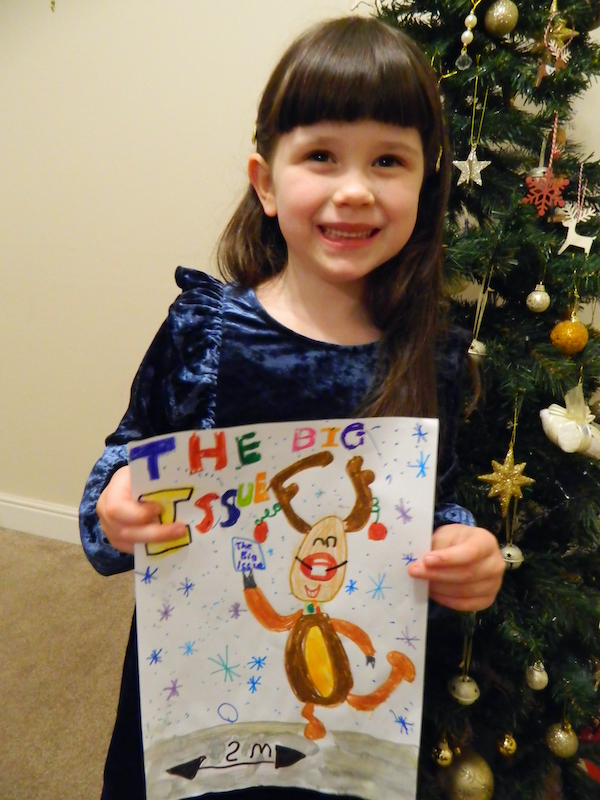 Evelyn, 5, holds her winning Christmas cover entry in front of a Christmas tree