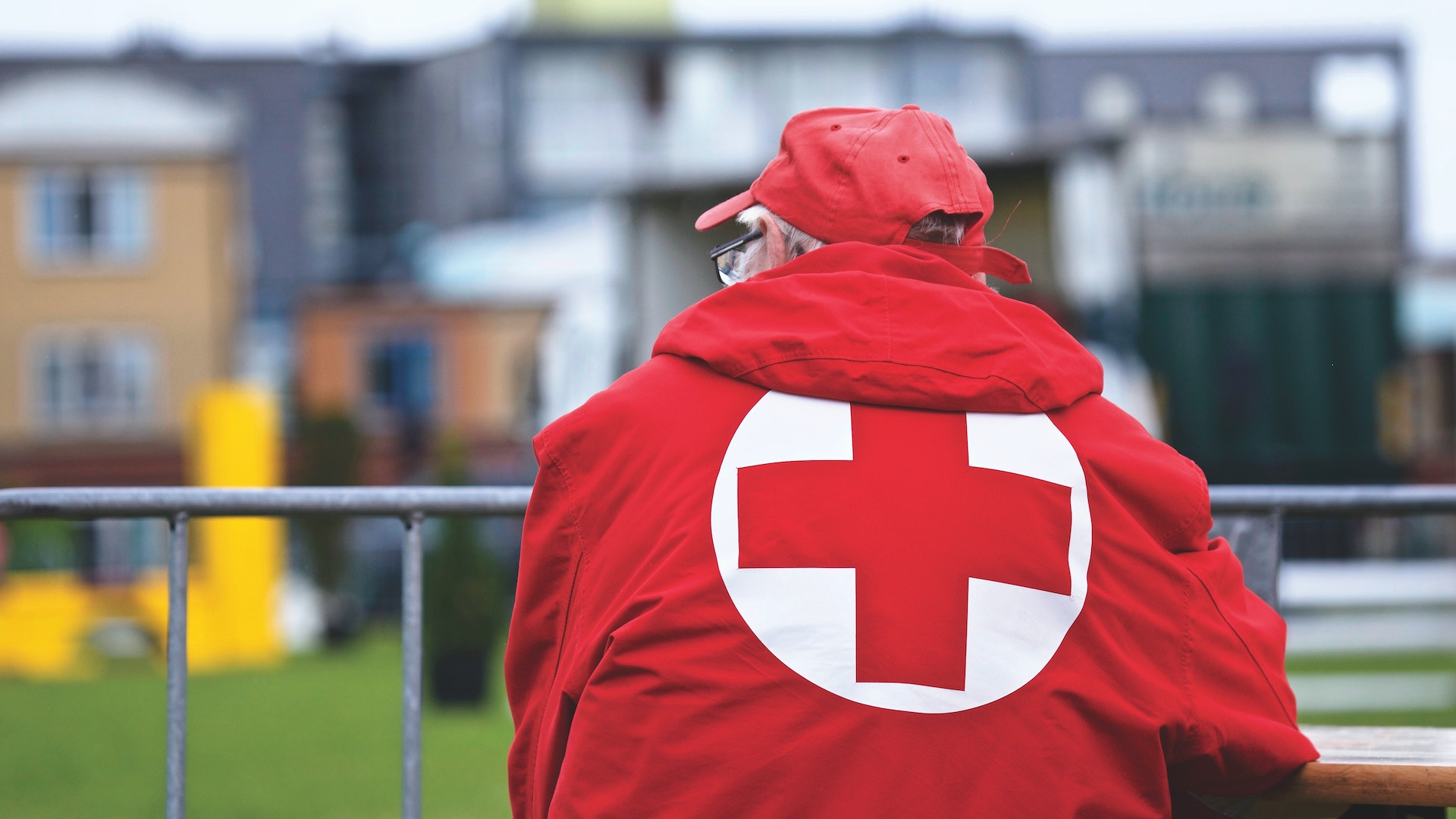 A man in a red cross jackert leans on a railing