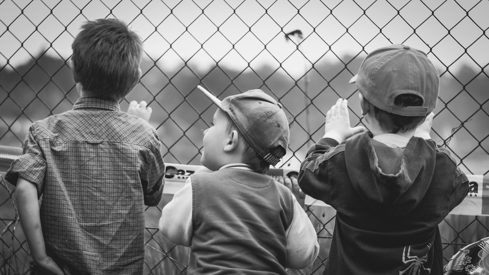 Three boys stand against a chain link fence