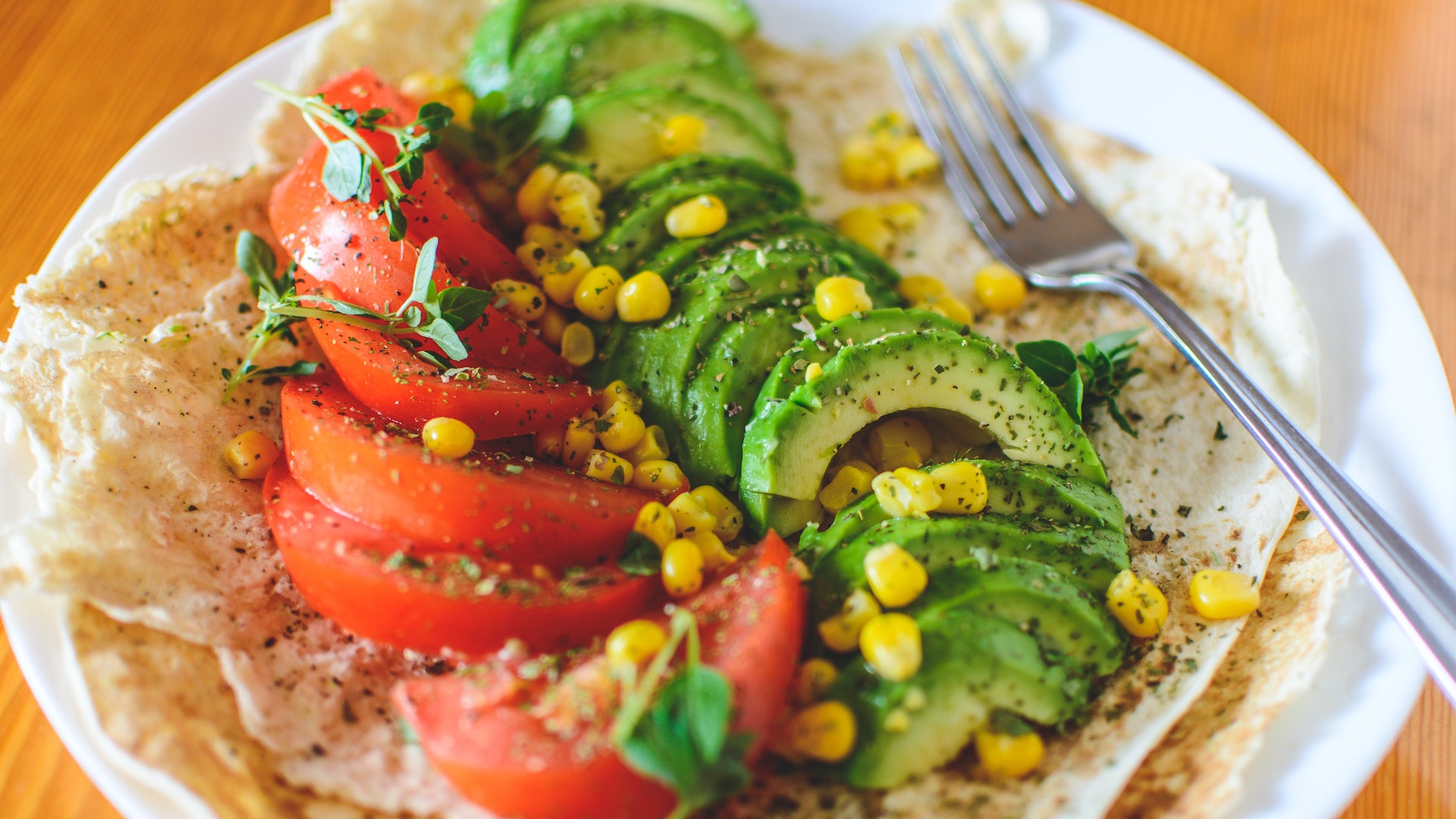 Slices of seasoned tomato and avocado sit on a wrap