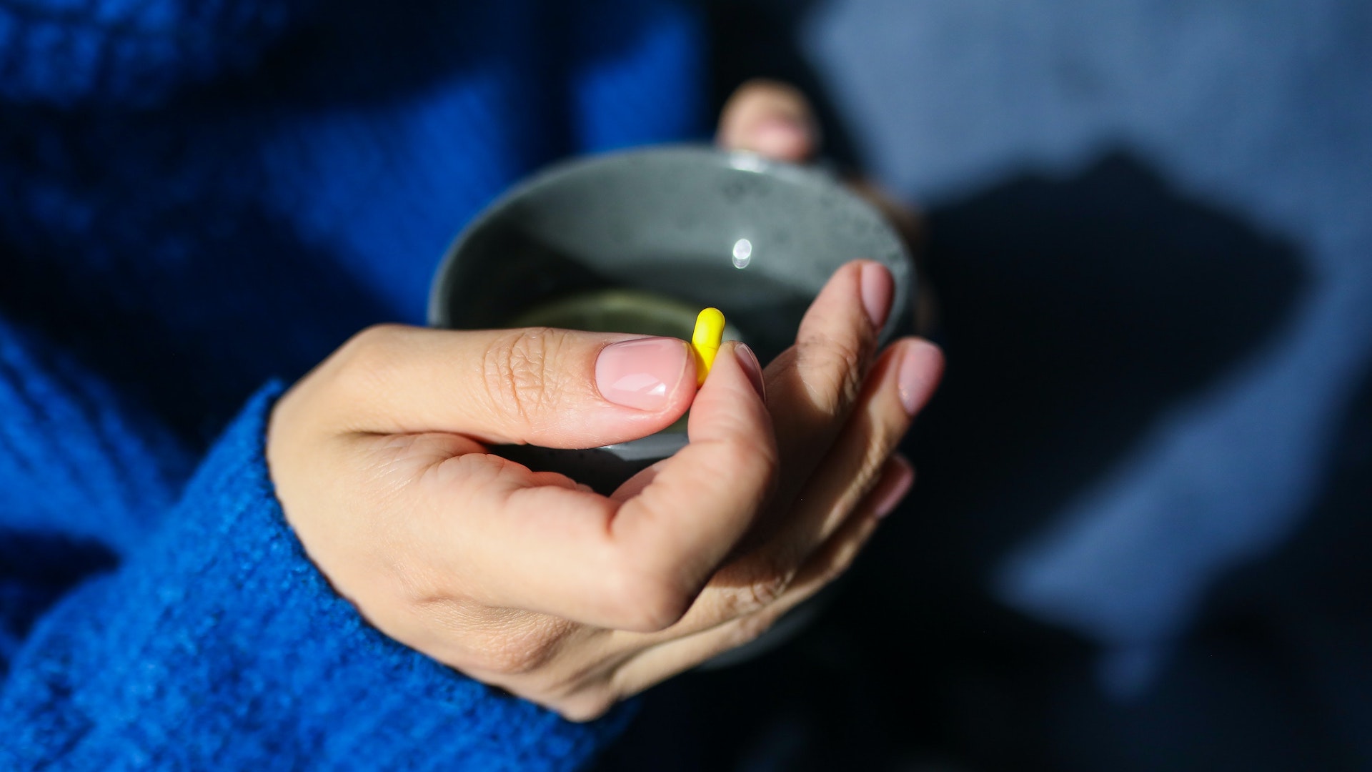 A woman's hand holding a mug, about to take a pill. Universal credit cut