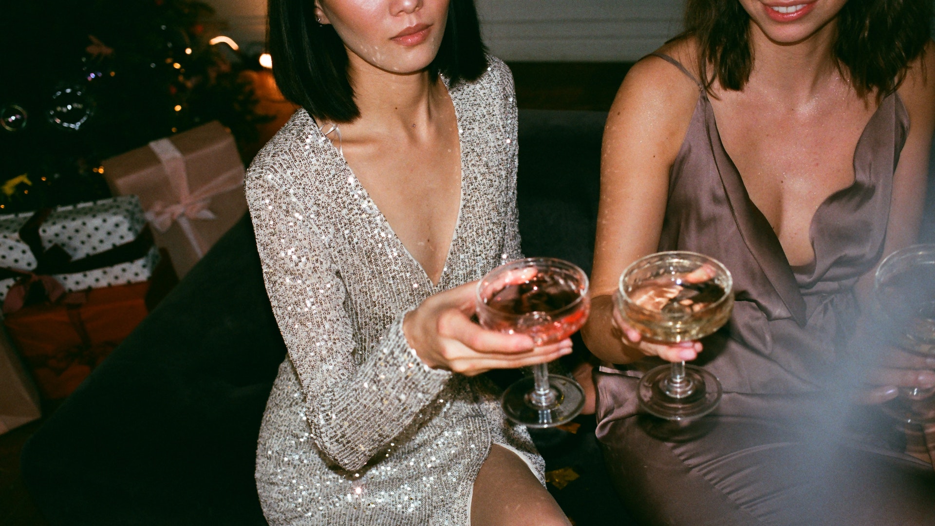 Two women hold wine glasses wearing glamourous dresses