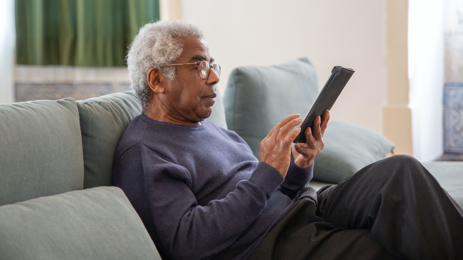 An older man sits on a couch looking at an iPad. Pension triple lock
