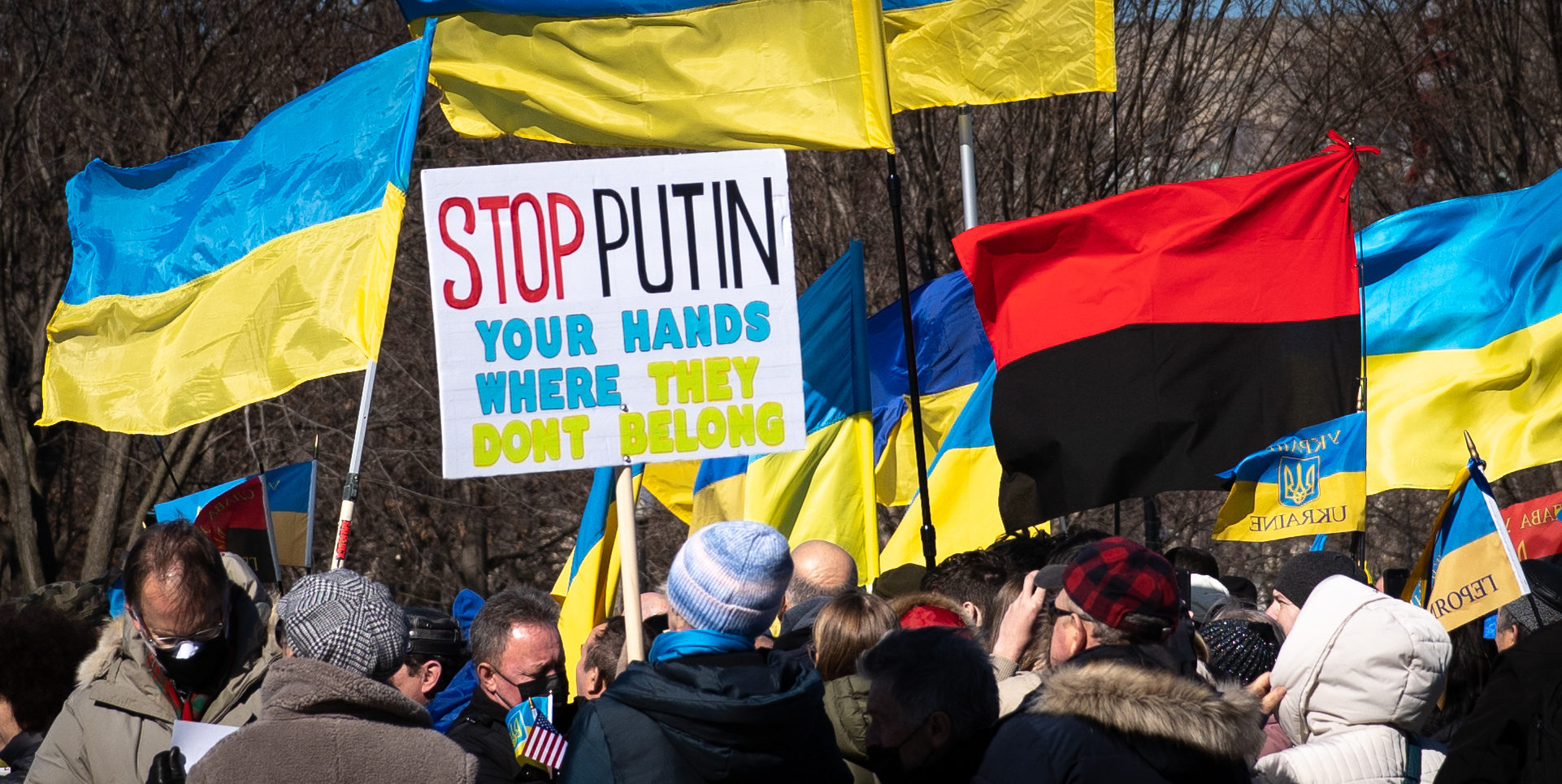 Rally against war in Ukraine with flags and sign reading "Stop Putin your hands where they don't belong"