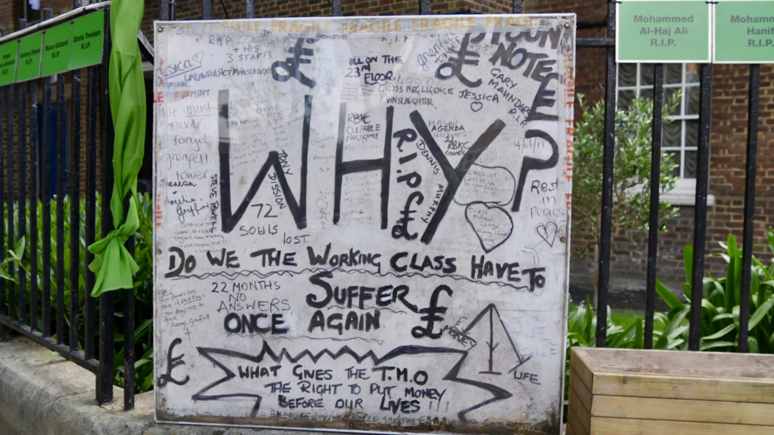 Handwritten sign sits on the corner of Bramley Road, leading to Grenfell Tower. It states "Why do we, the working class, have to suffer once again?"