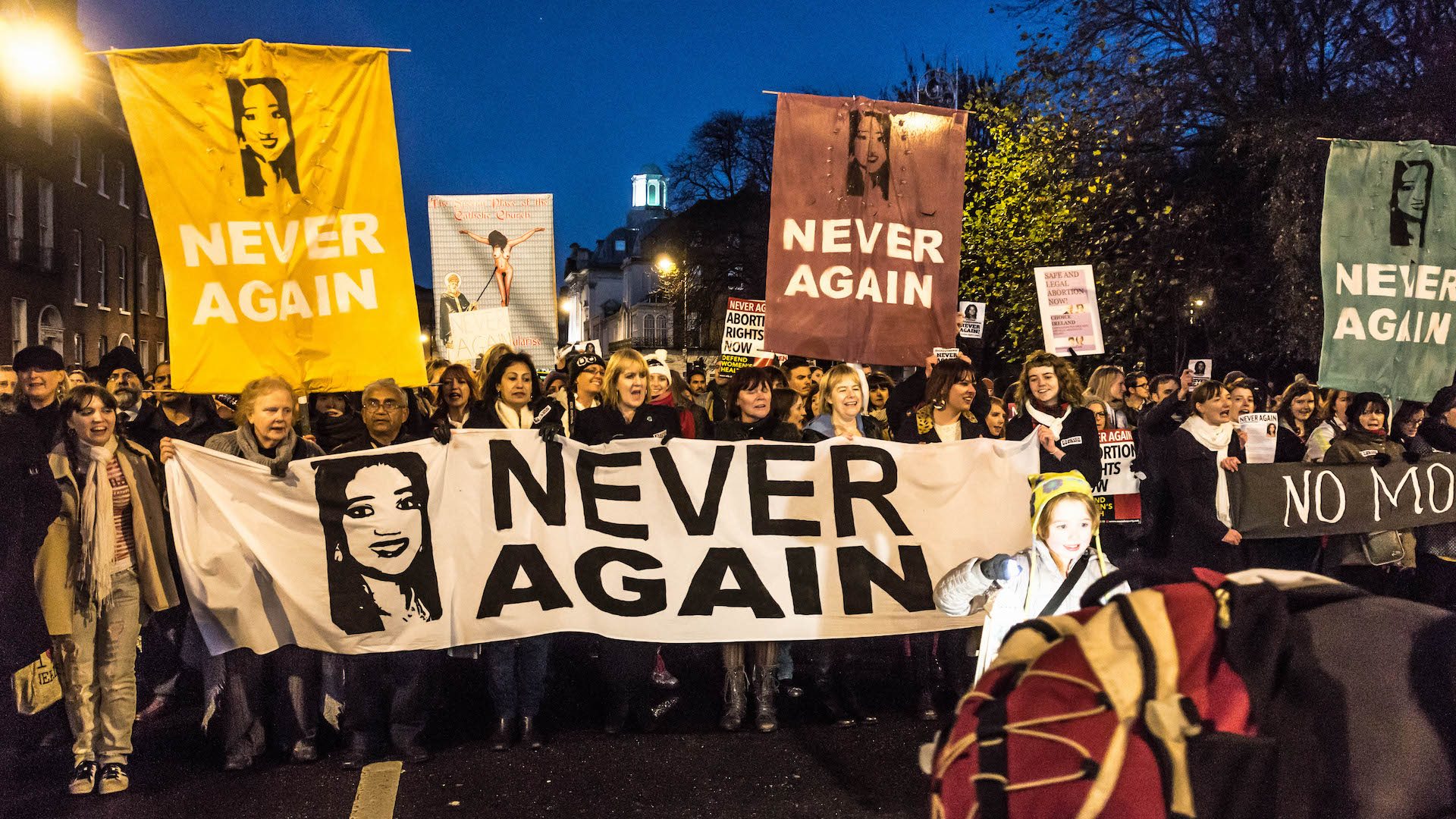 Women march holding banners and signs saying "never again"