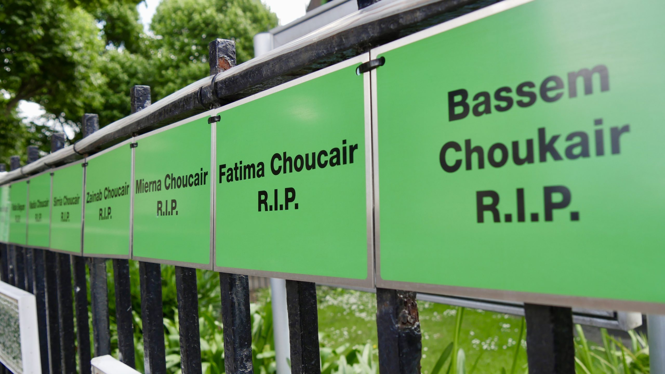 Green metal signs state the names of those who lost their lives in the fire that hang on the railings near Grenfell Tower