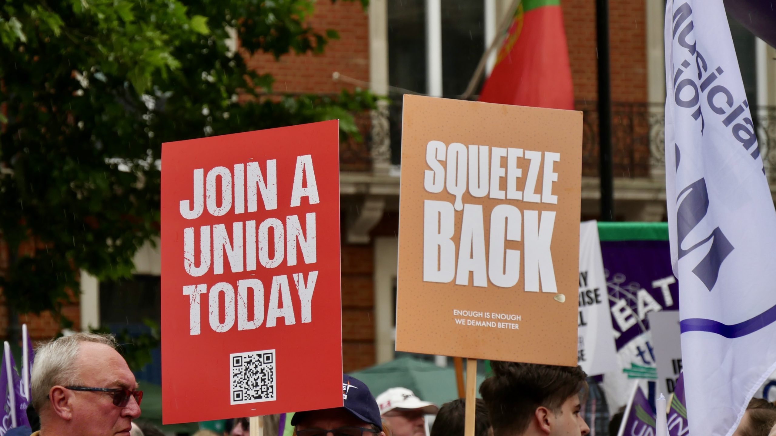 Signs that read "Join a union today" and "Squeeze back" are held up by protestors