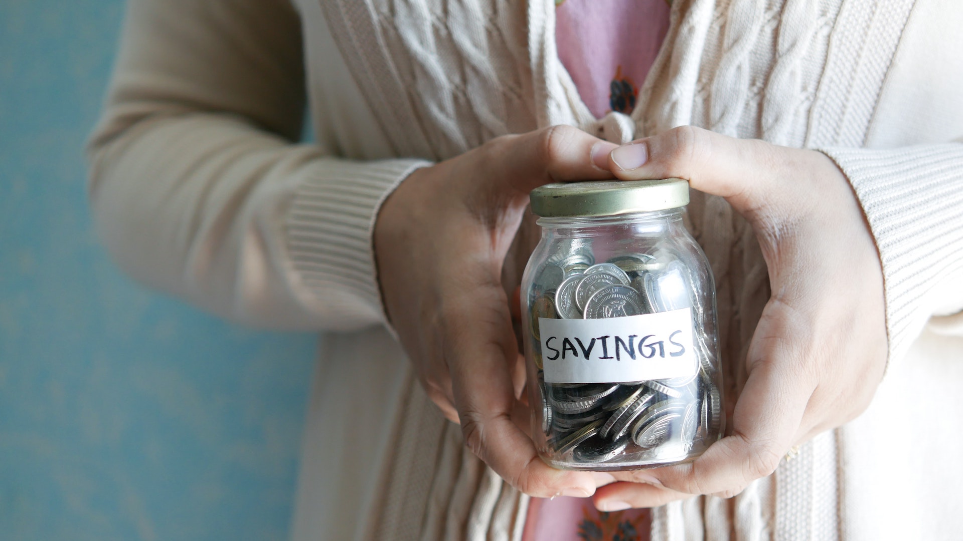 A woman holds a glass jar marked "savings" with pennies in it