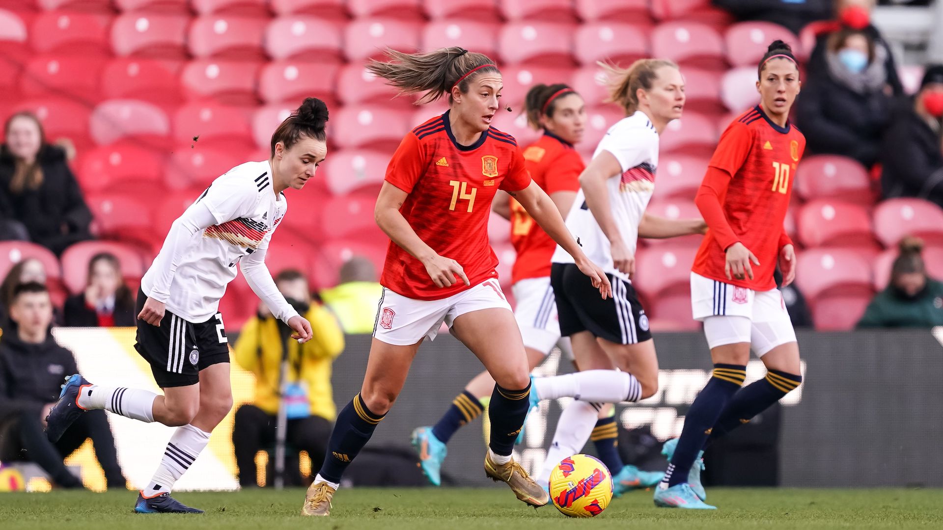 Alexia Putellas in the red shirt of spain kicks the ball with german players in white in the background
