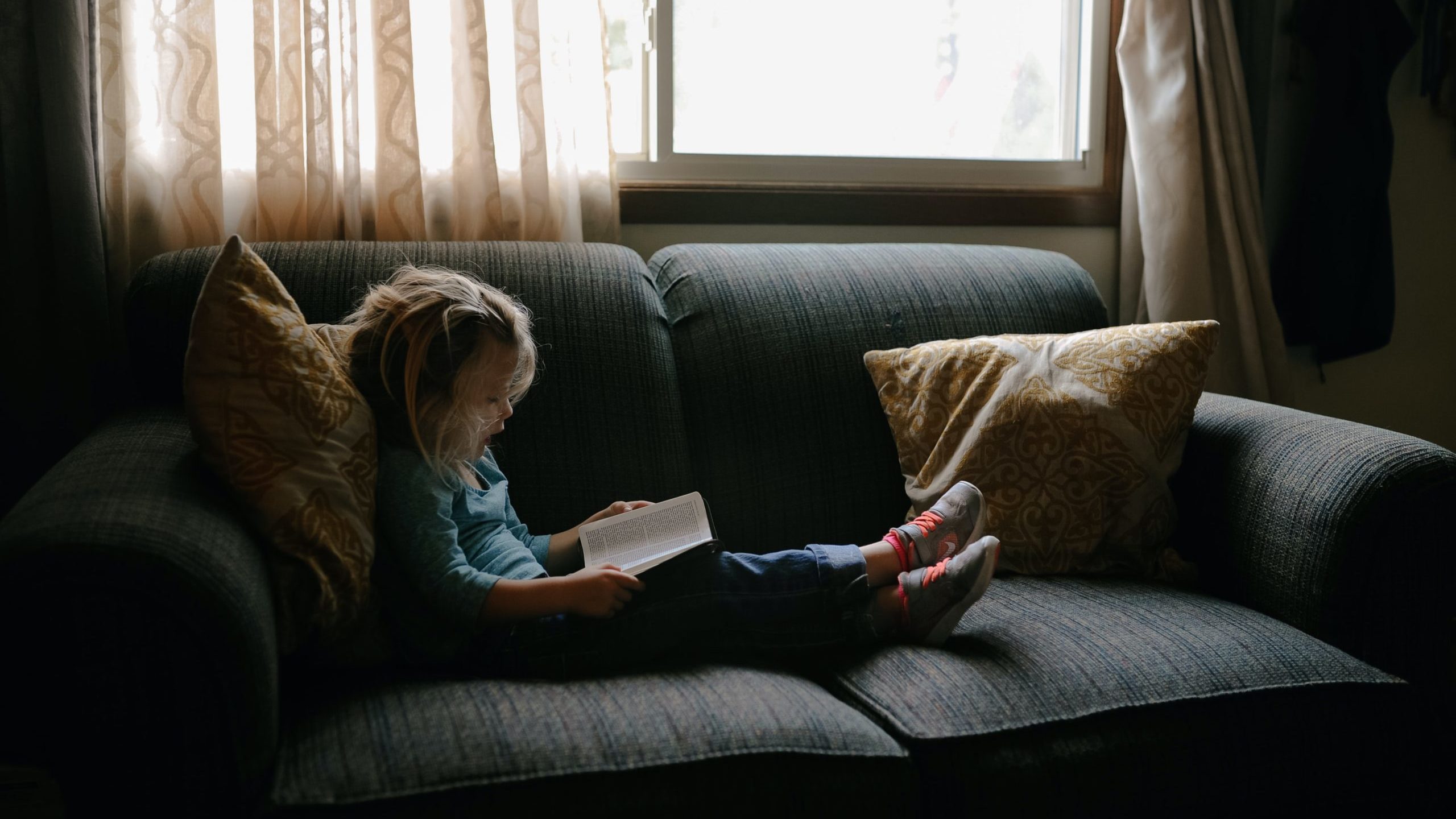 child reading a book on a sofa