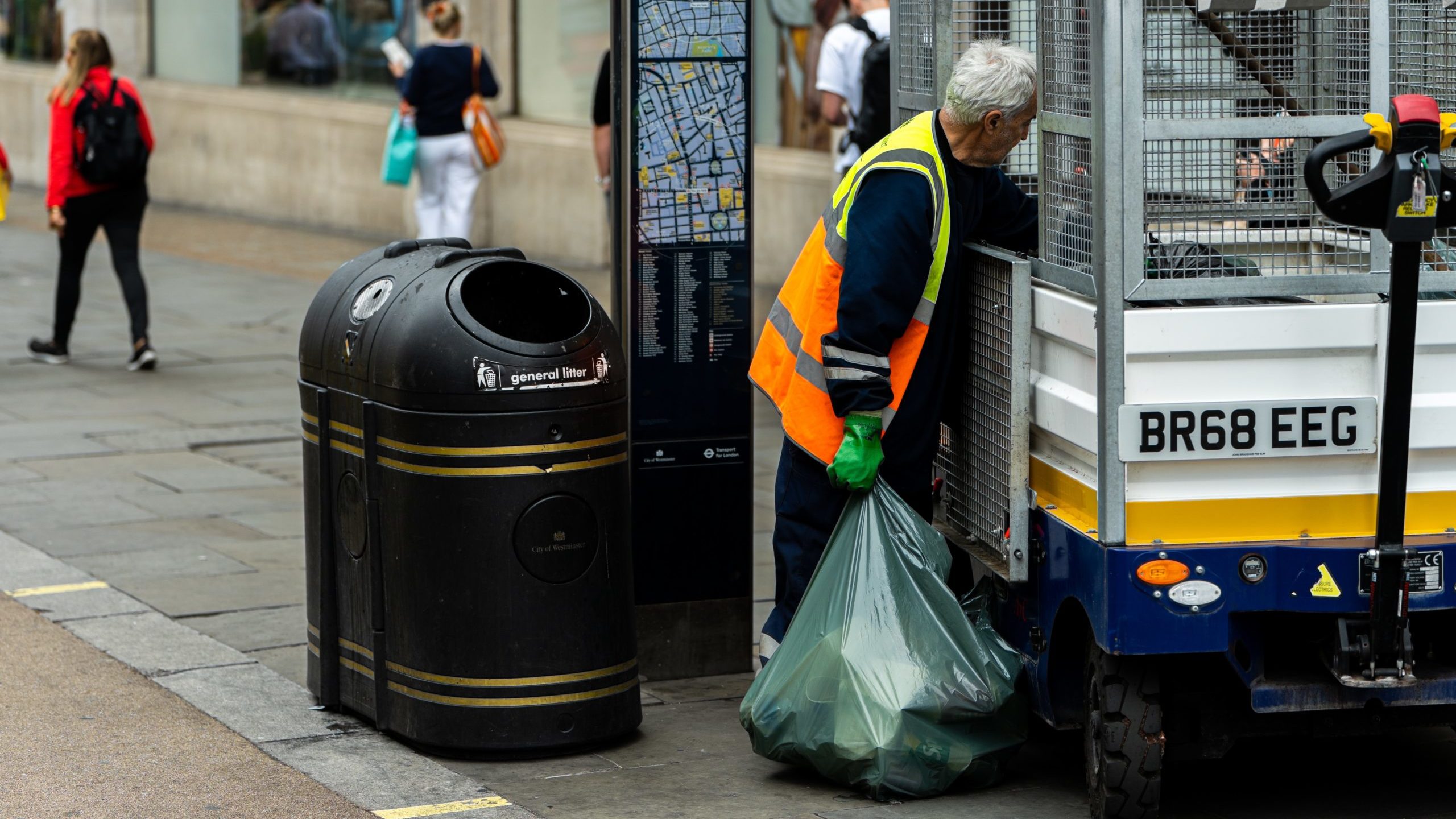 A street cleaner collects a bag of waste from a public bin.