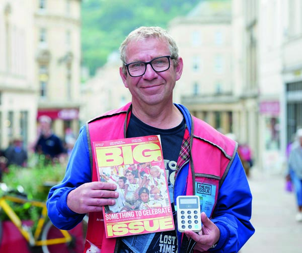 Big Issue vendor Ian Duff stands with a copy of the magazine and his card reader