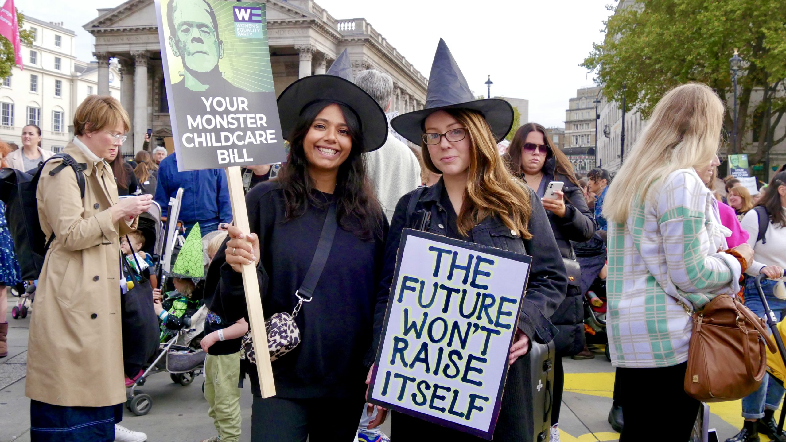 Two mothers in witch costumes hold sign: 'The future won't raise itself'
