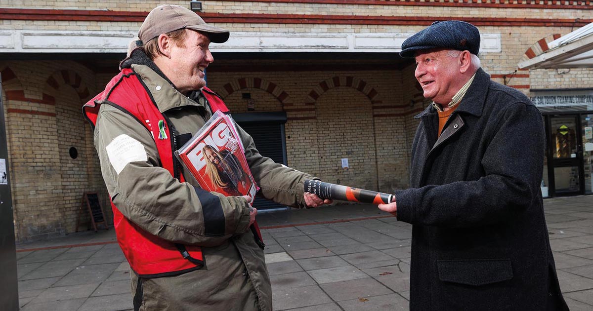 A Big Issue Vendor takes a contactless payment from a customer