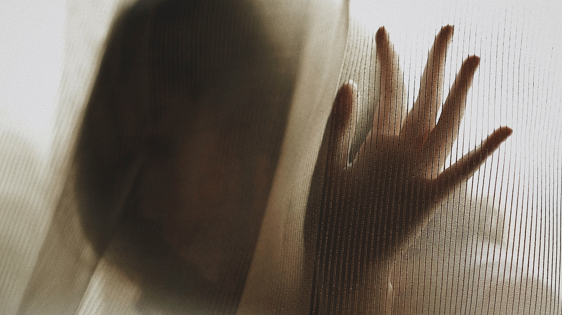A face and a hand obscured by a curtain