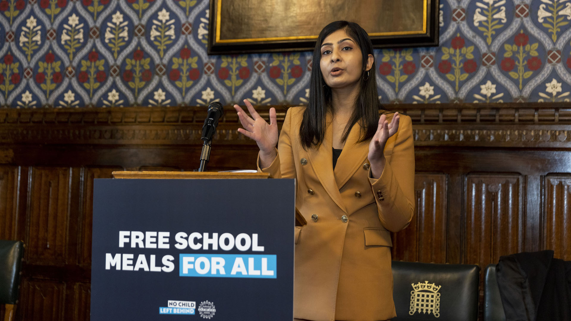 Zarah Sultana gives a speech standing behind a lectern with "free school meals for all" on it