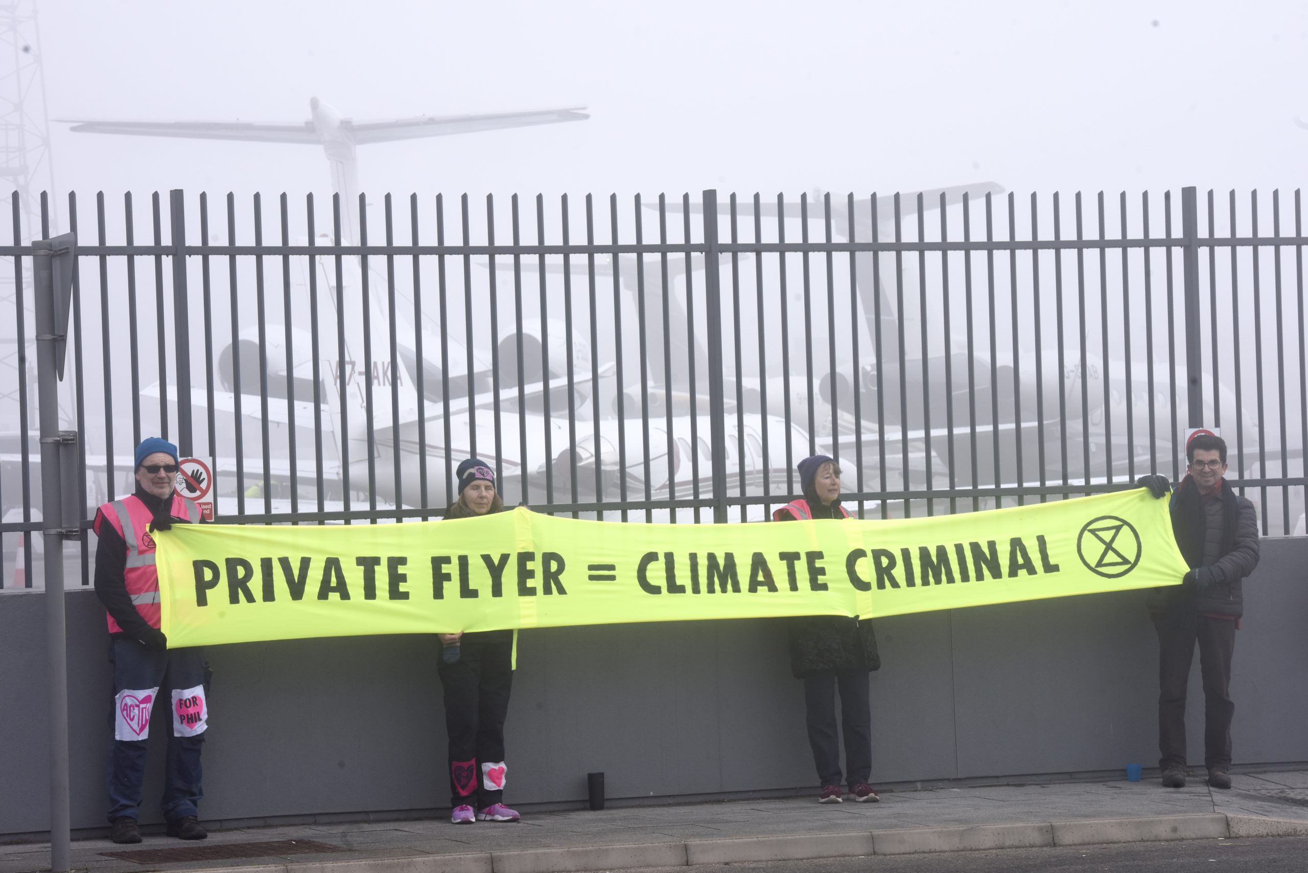 Extinction Rebellion protesters stand at Luton Airport holding a sign reading "private flyer = climate criminal"