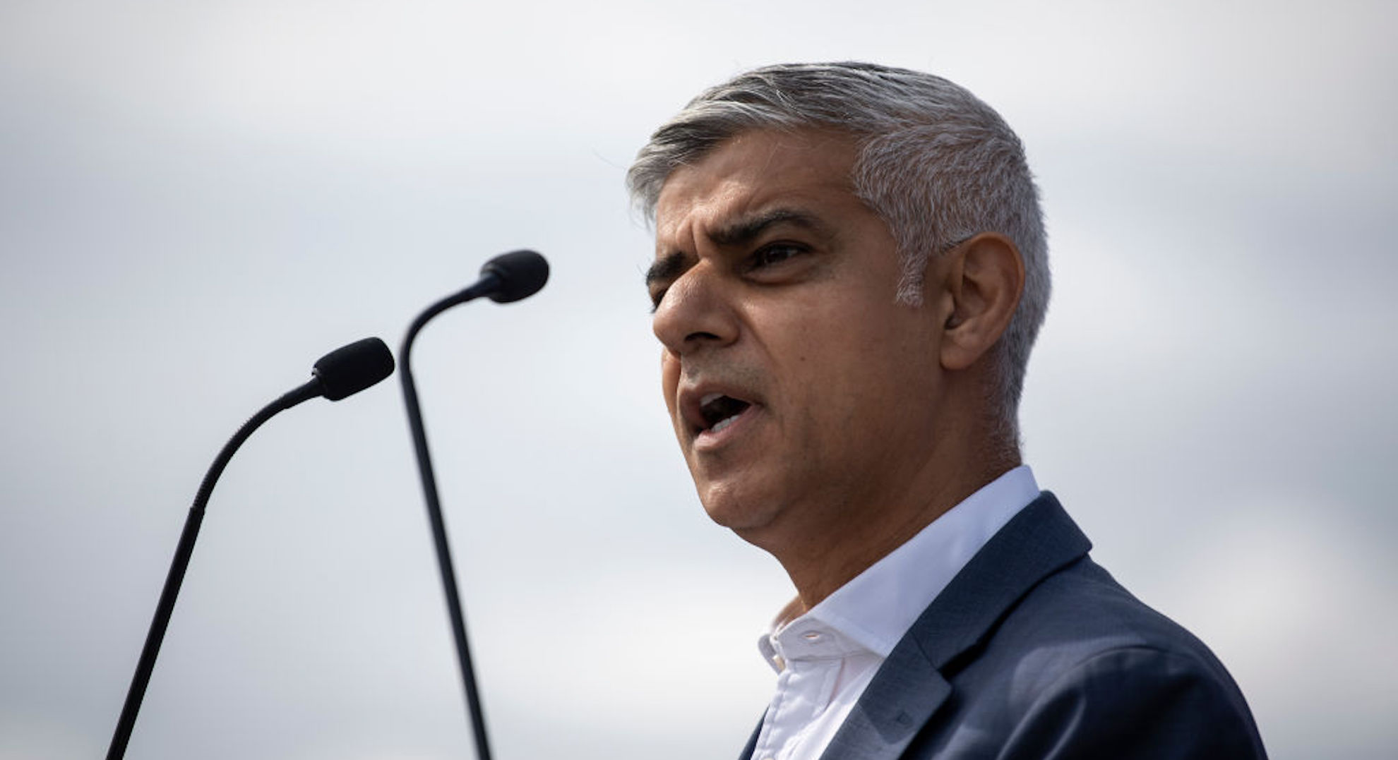 Mayor Sadiq Khan speaking at a podium for the 10th anniversary of the Olympics with a microphone in his face