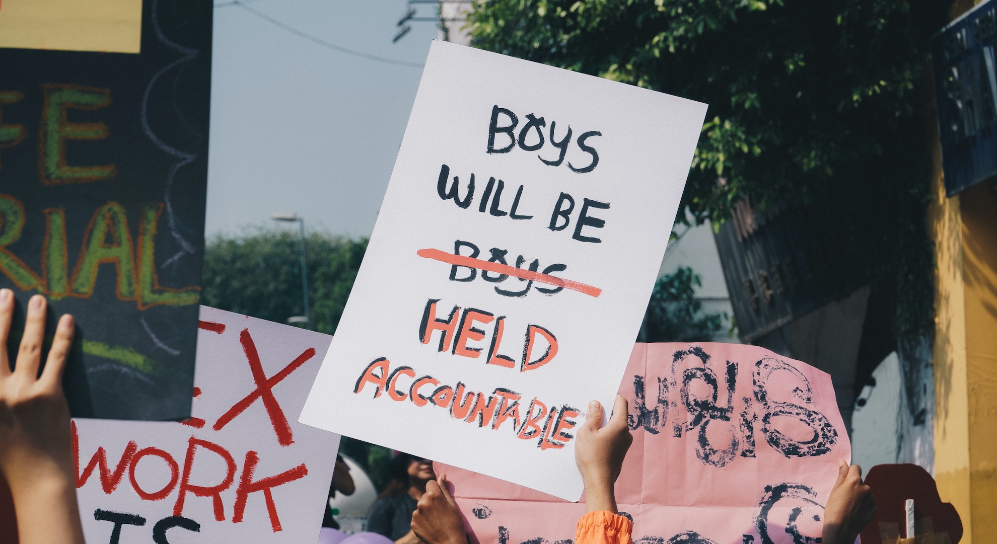 Women's march in Malaysia with protest sign that says boys will be boys but the second boys is struck out and replaced with 'held accountable' instead to fight against misogyny and abuse and for equality, which is what many people speak on for International Women's Day.