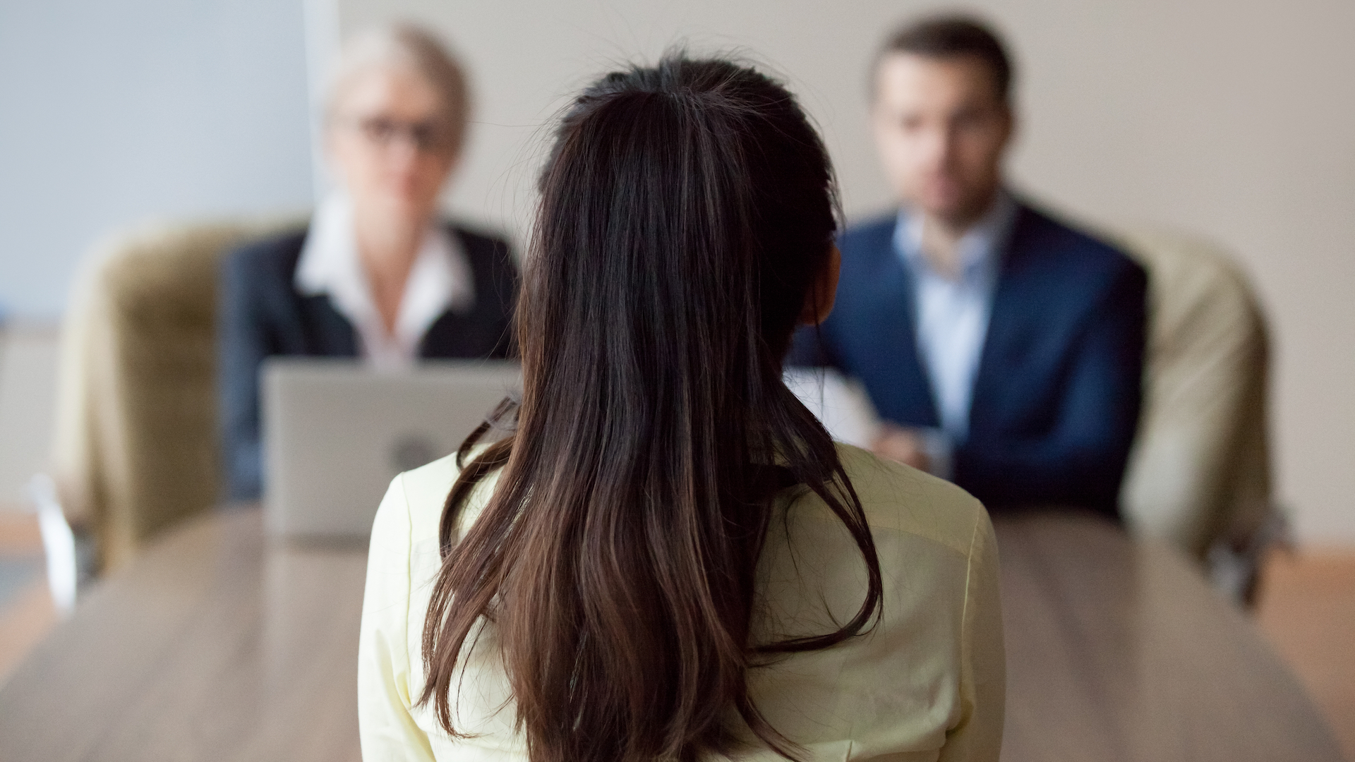 Businesswoman and businessman HR manager interviewing woman. Candidate female sitting her back to camera, focus on her, close up rear view, interviewers on background