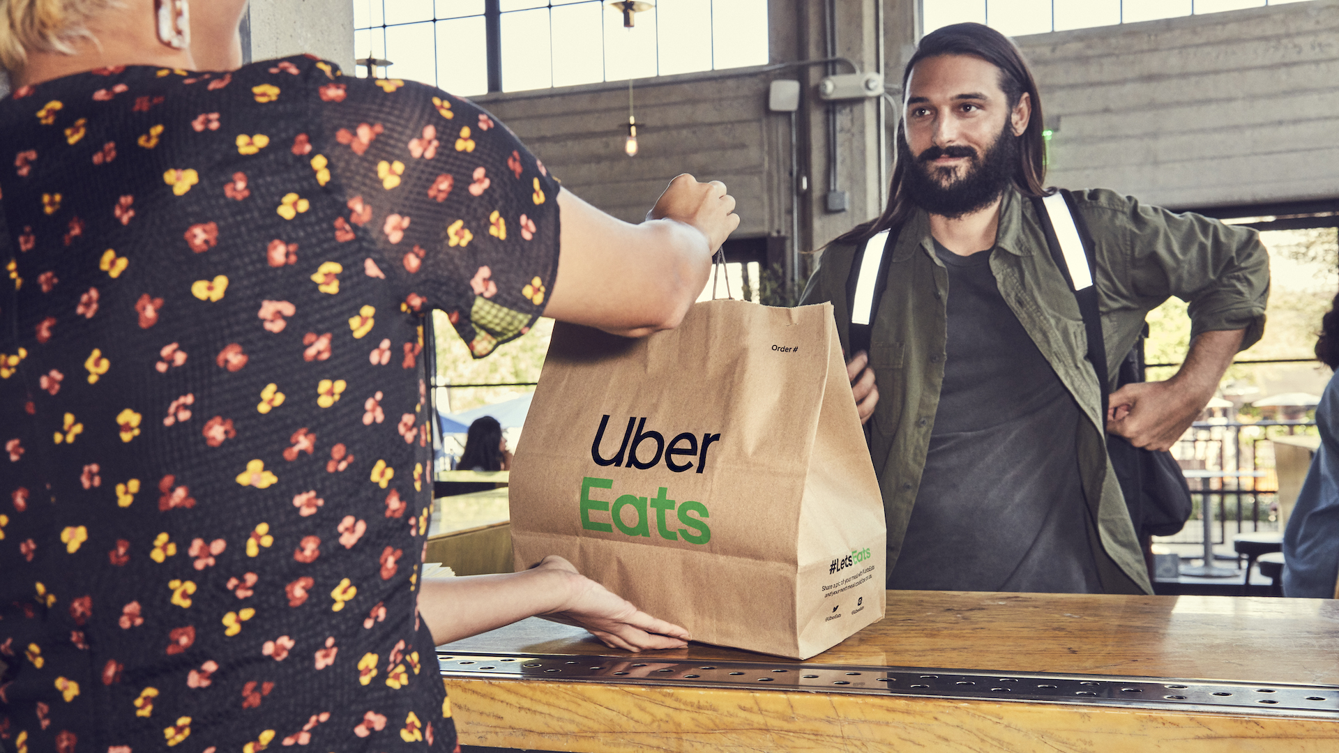 a man aproaches a restaurant counter with a paper bag saying "uber eats"