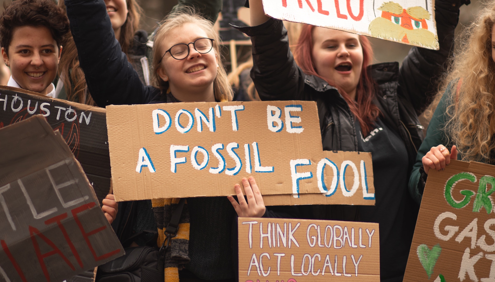 Young people at a climate protest in birmingham with a sign that says "don't be a fossil fool" and "think globally act locally"