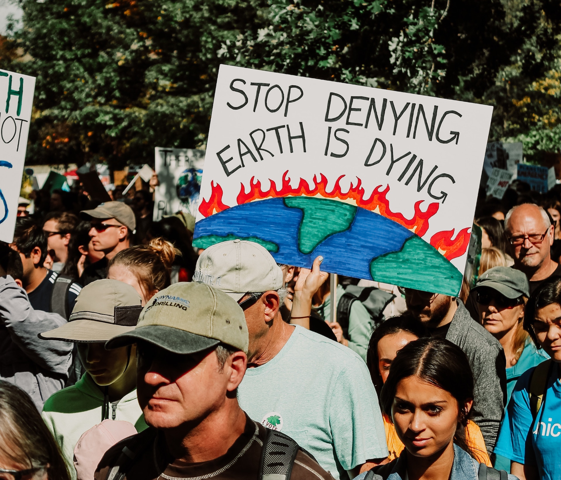 People standing at a climate change protest with one person holding up a sign that says "stop denying earth is dying" to combat climate misinformation