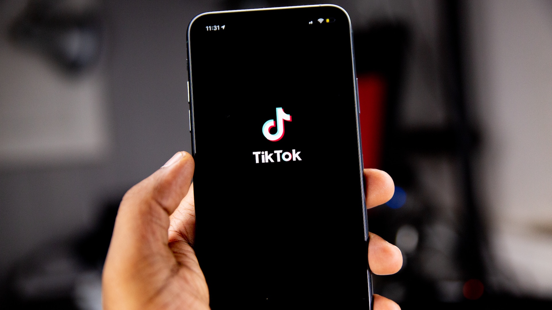 white hand holding an iphone with a black screen and a TikTok logo