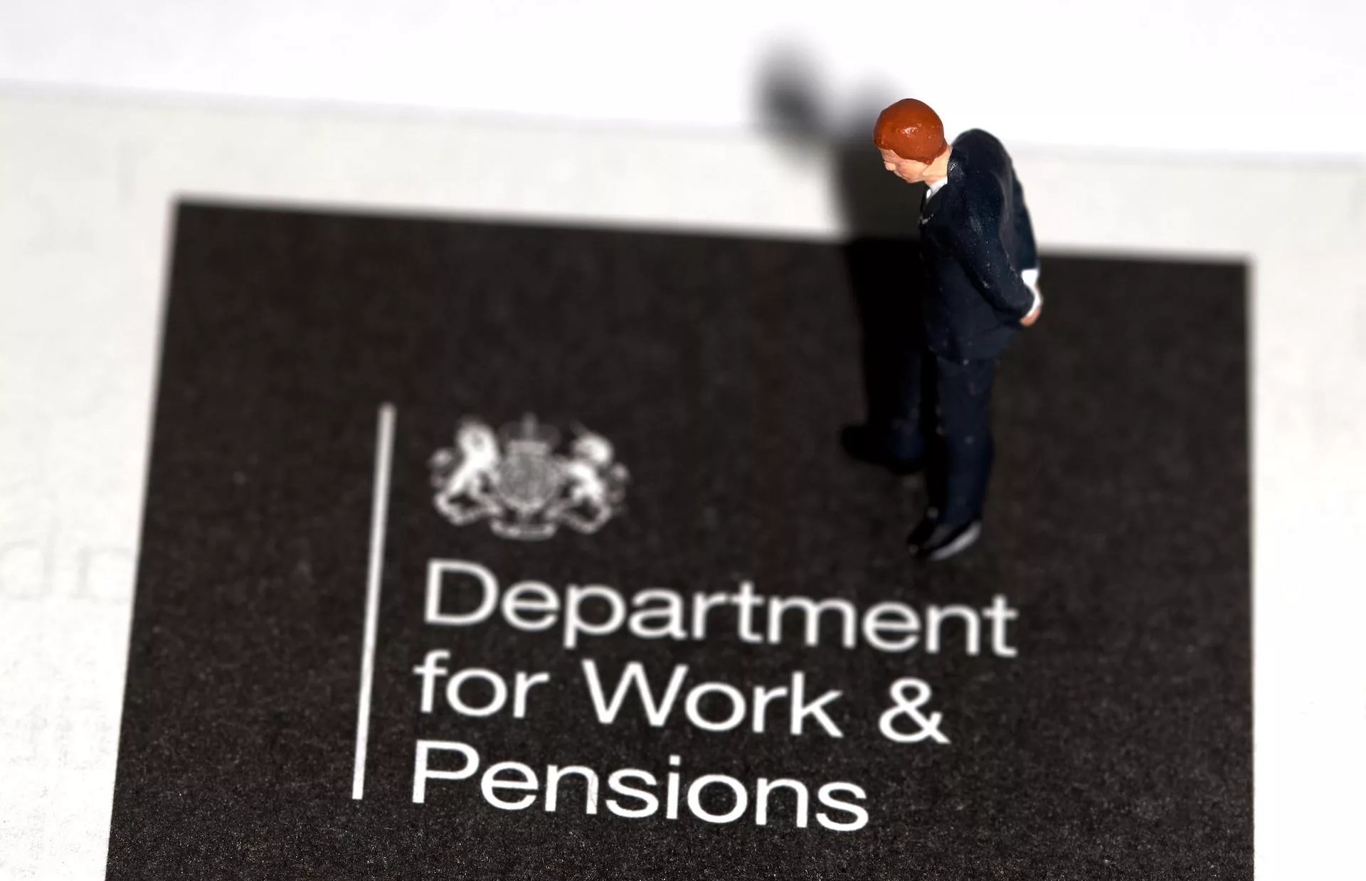 A miniature figurine businessman looking down on an information booklet for department for work and pensions
