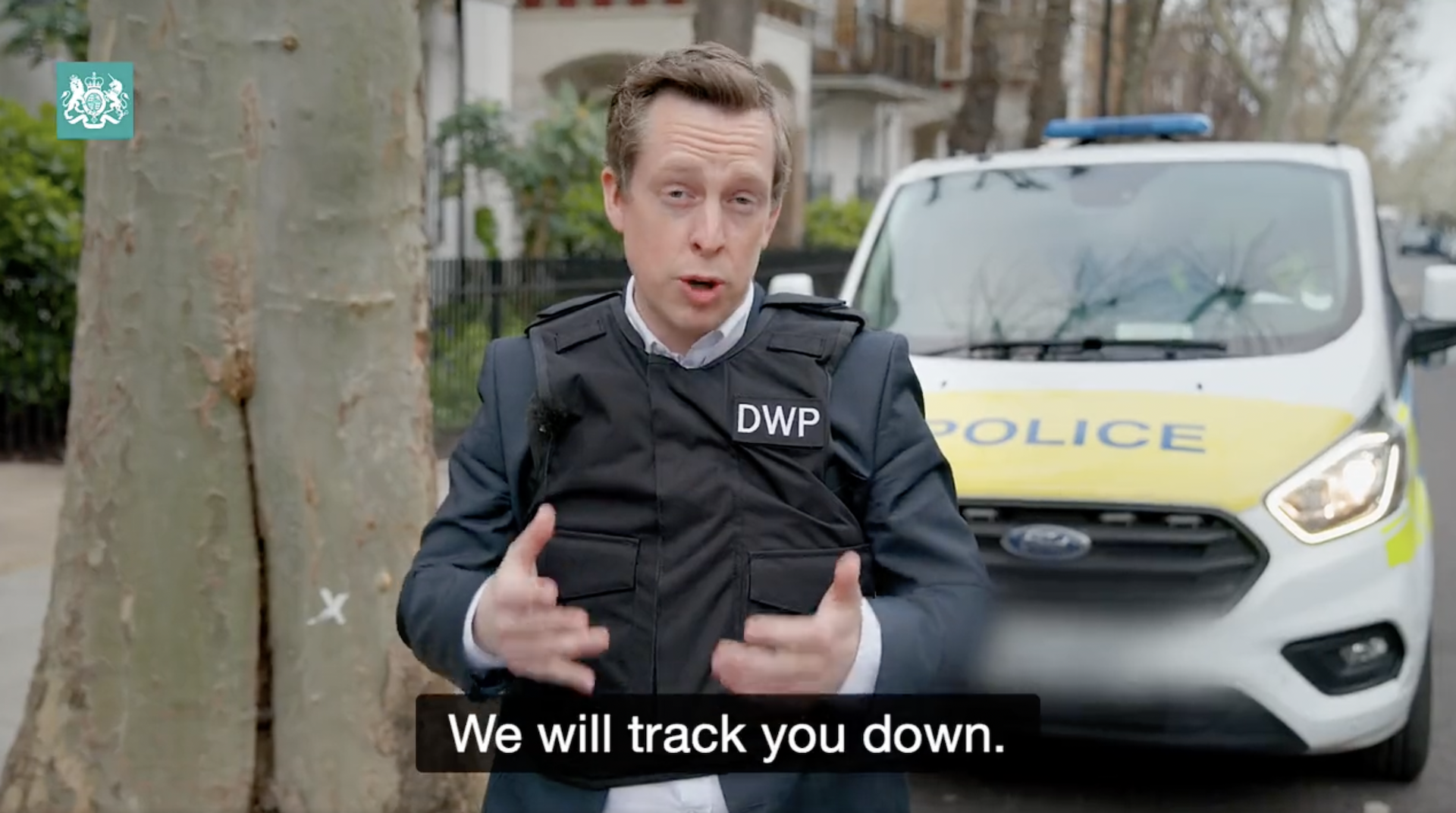 Disability minister Tom Pursglove wears a stab vest with a DWP badge in front of police car