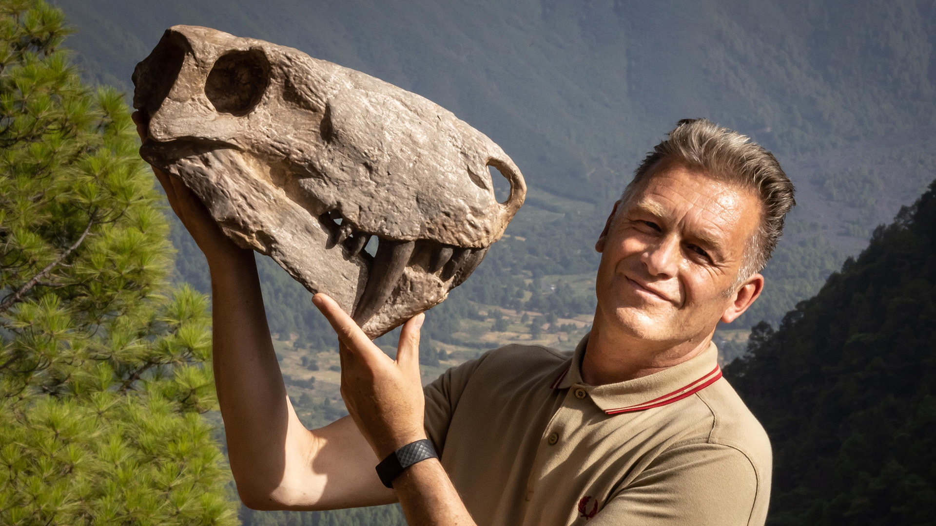 Chris Packham holding a dinosaur skull and smiling