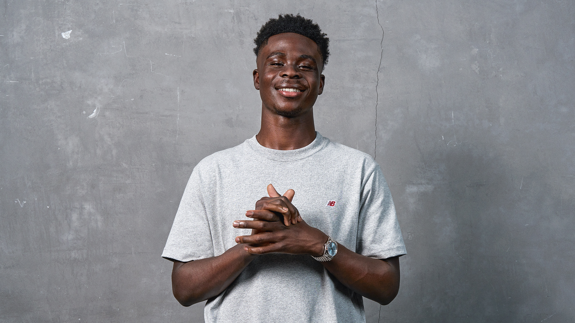 Bukayo Saka in a white t-shirt, hands clasped together