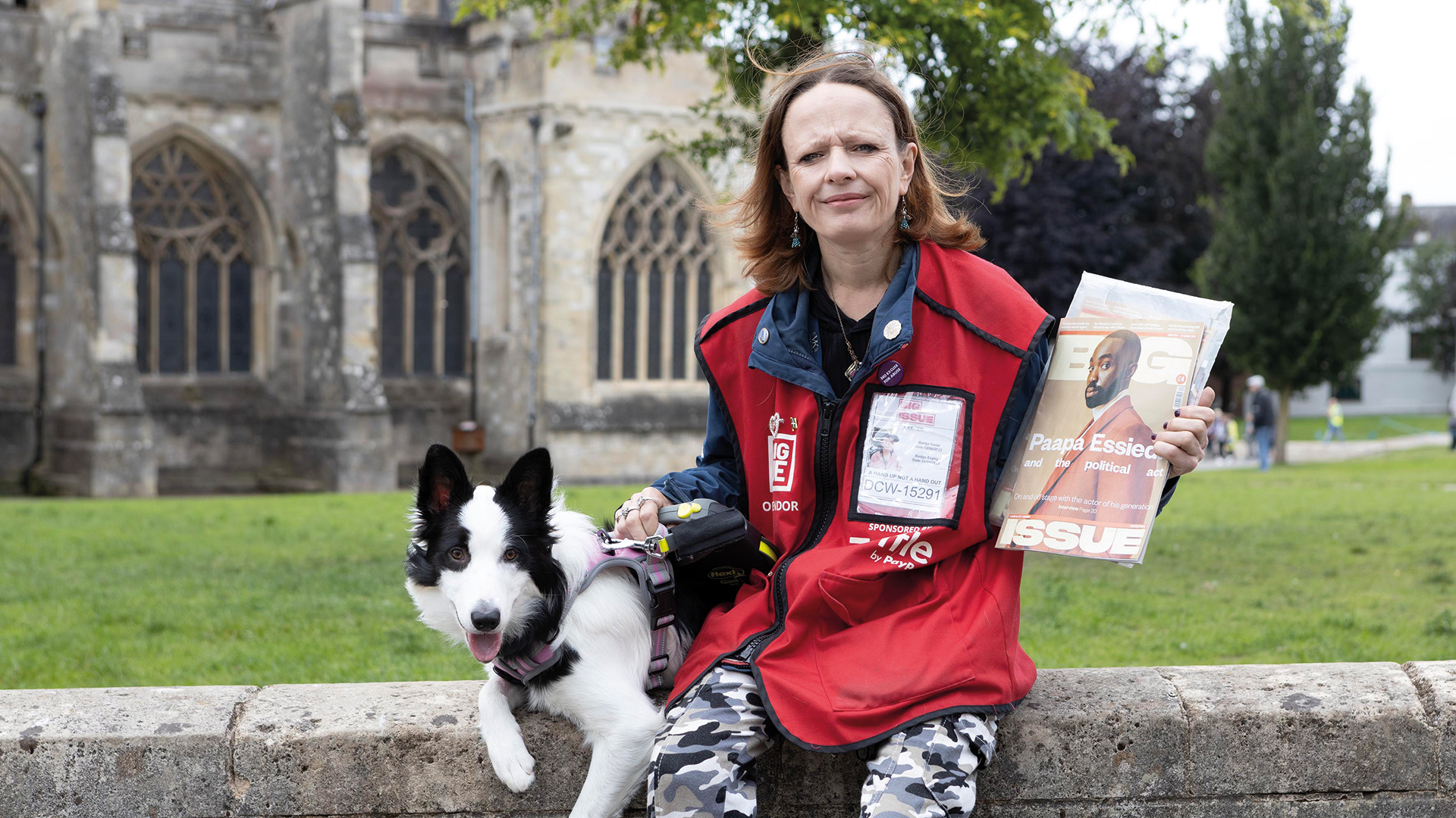 A big issue vendor and her black and white dog outside a church