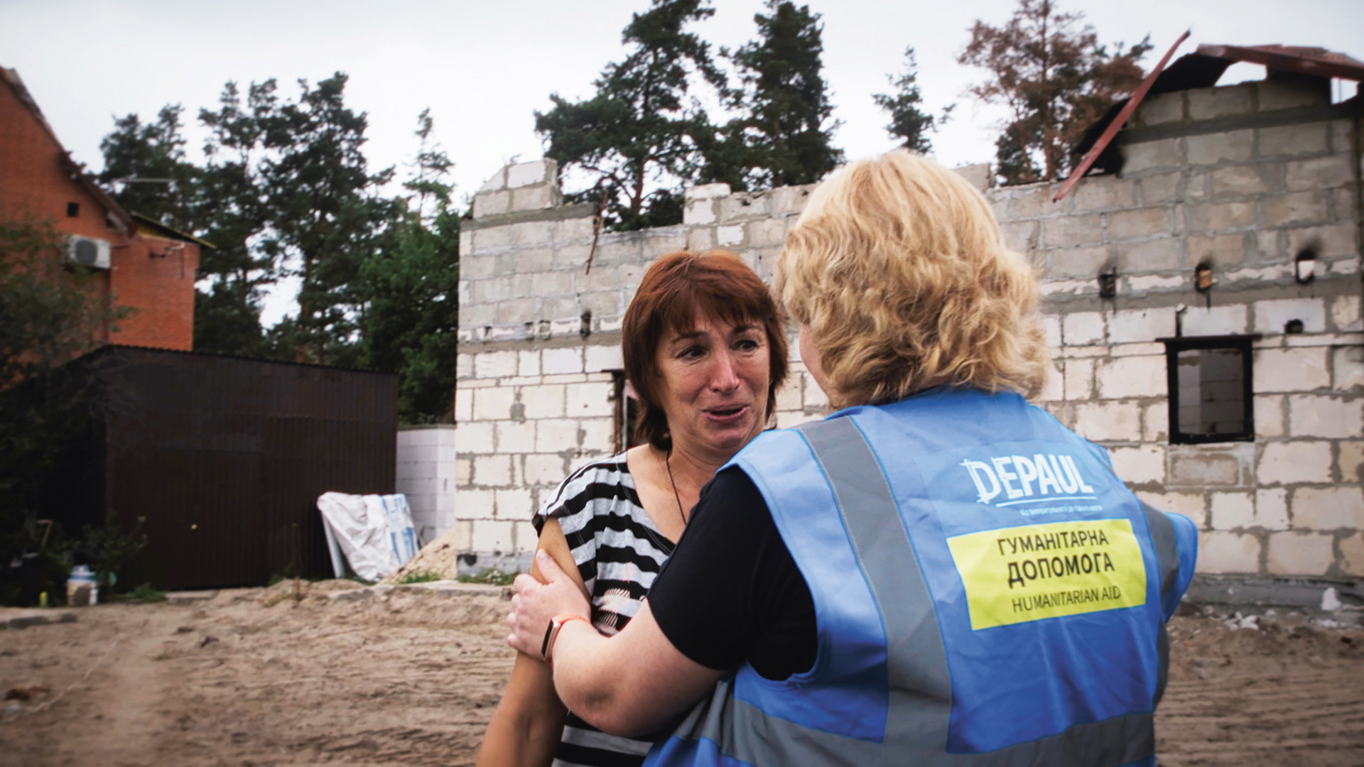 A woman is comforted by a Depaul aid worker amid ruins