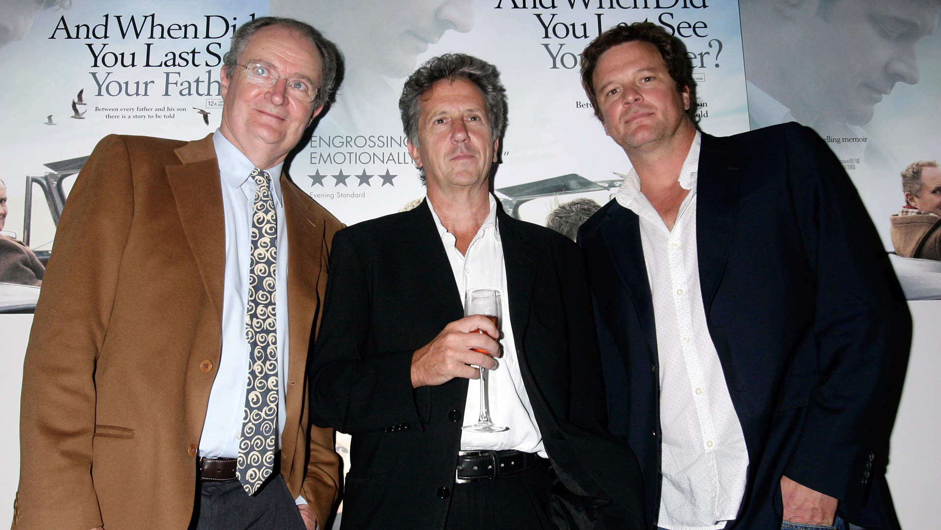 Jim Broadbent, Blake Morrison holding a glass of champagne and Colin Firth stand facing the camera