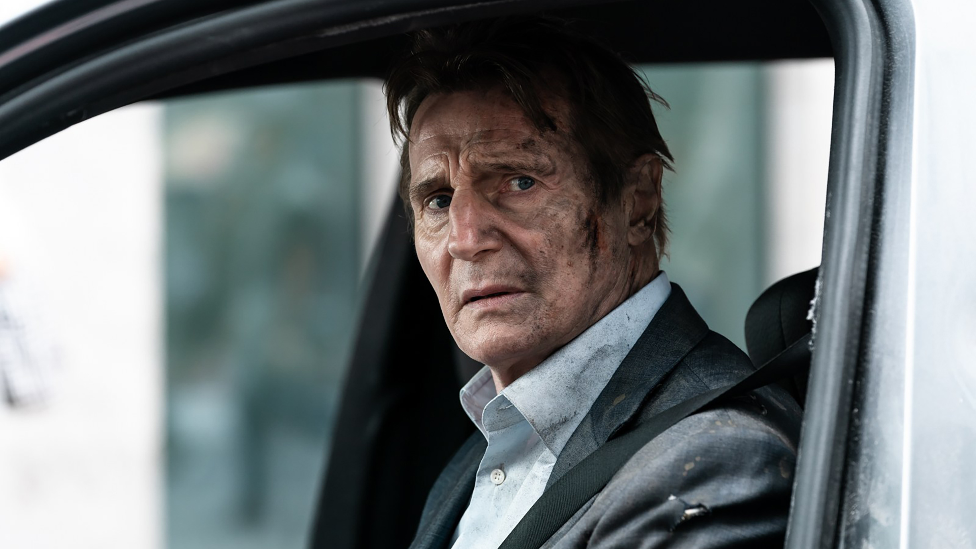 Liam Neeson looks out of a car window
